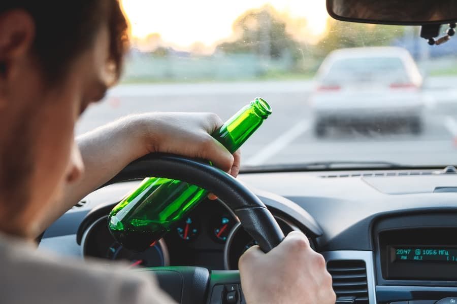 Wrecked bicycle, helmet, and eyeglasses on road in front of white car Young man driving with beer bottle in hand.
