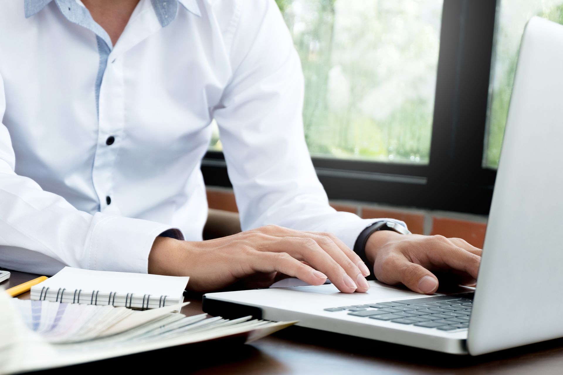 Collection agency professional typing on a laptop at a desk beside an open notebook.