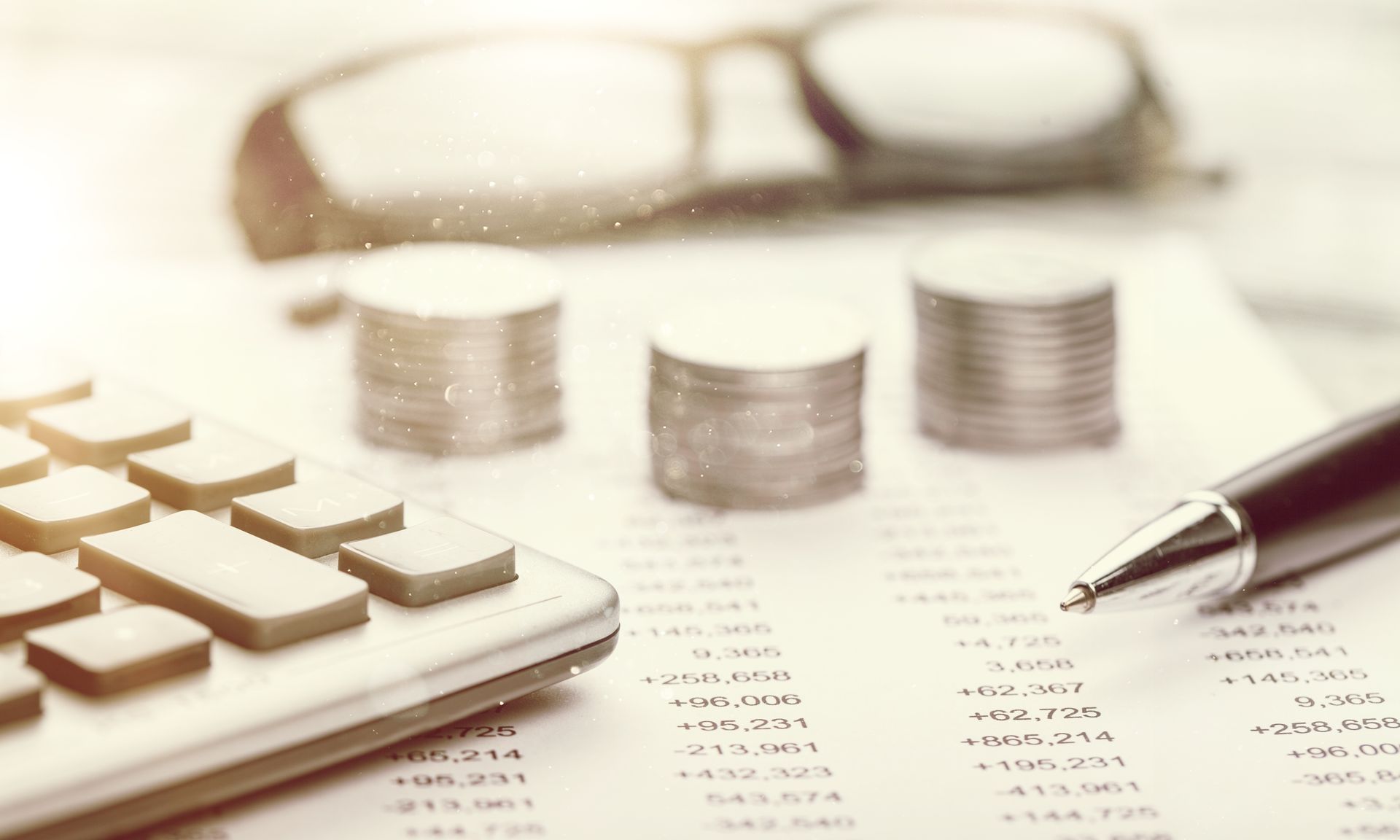 Close-up of a calculator next to a pair of piles of coins and a document. Close-up of a calculator next to a pair of piles of coins and a document.