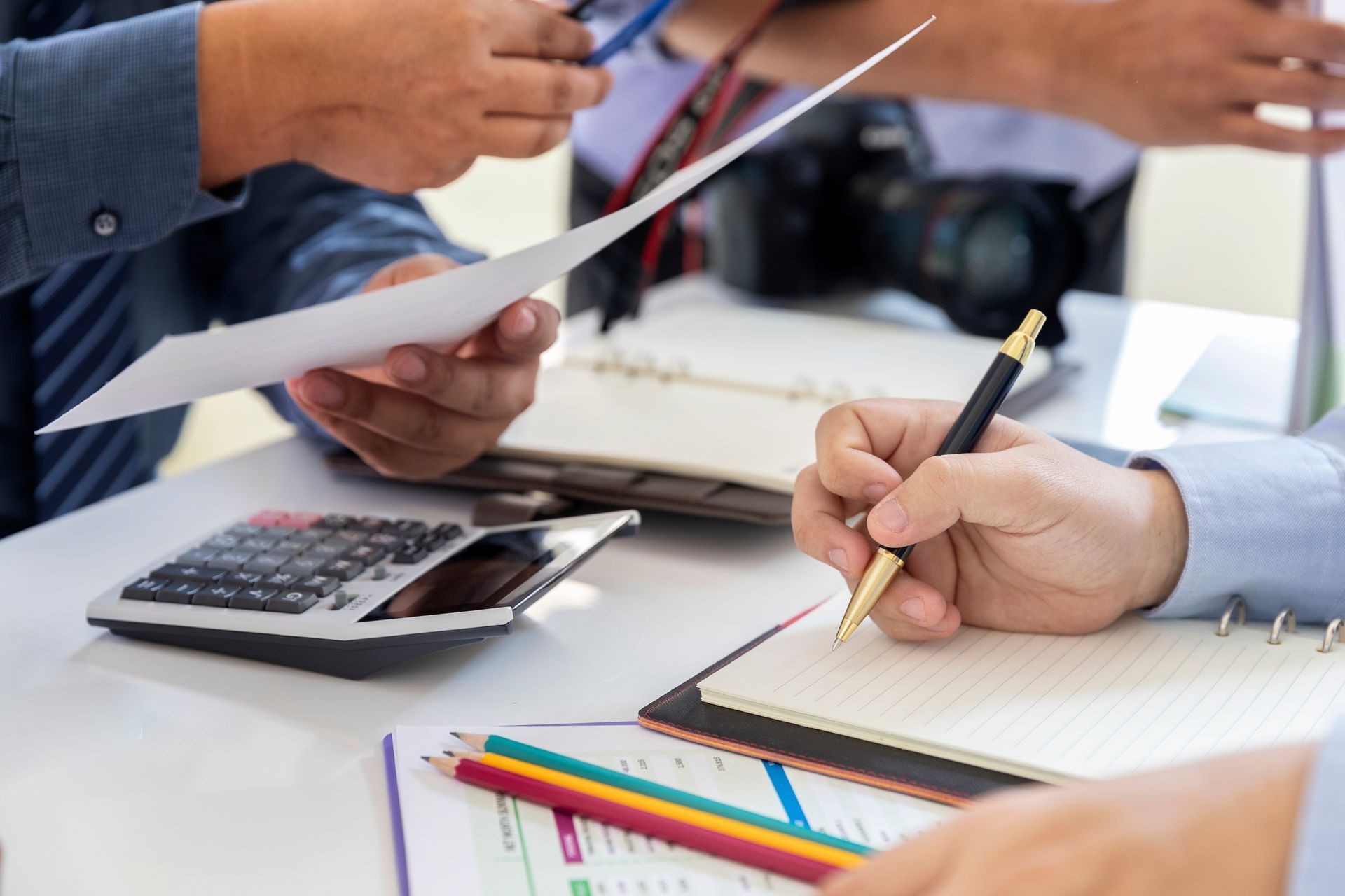 Business professionals reviewing paperwork and writing notes at a desk with a calculator.