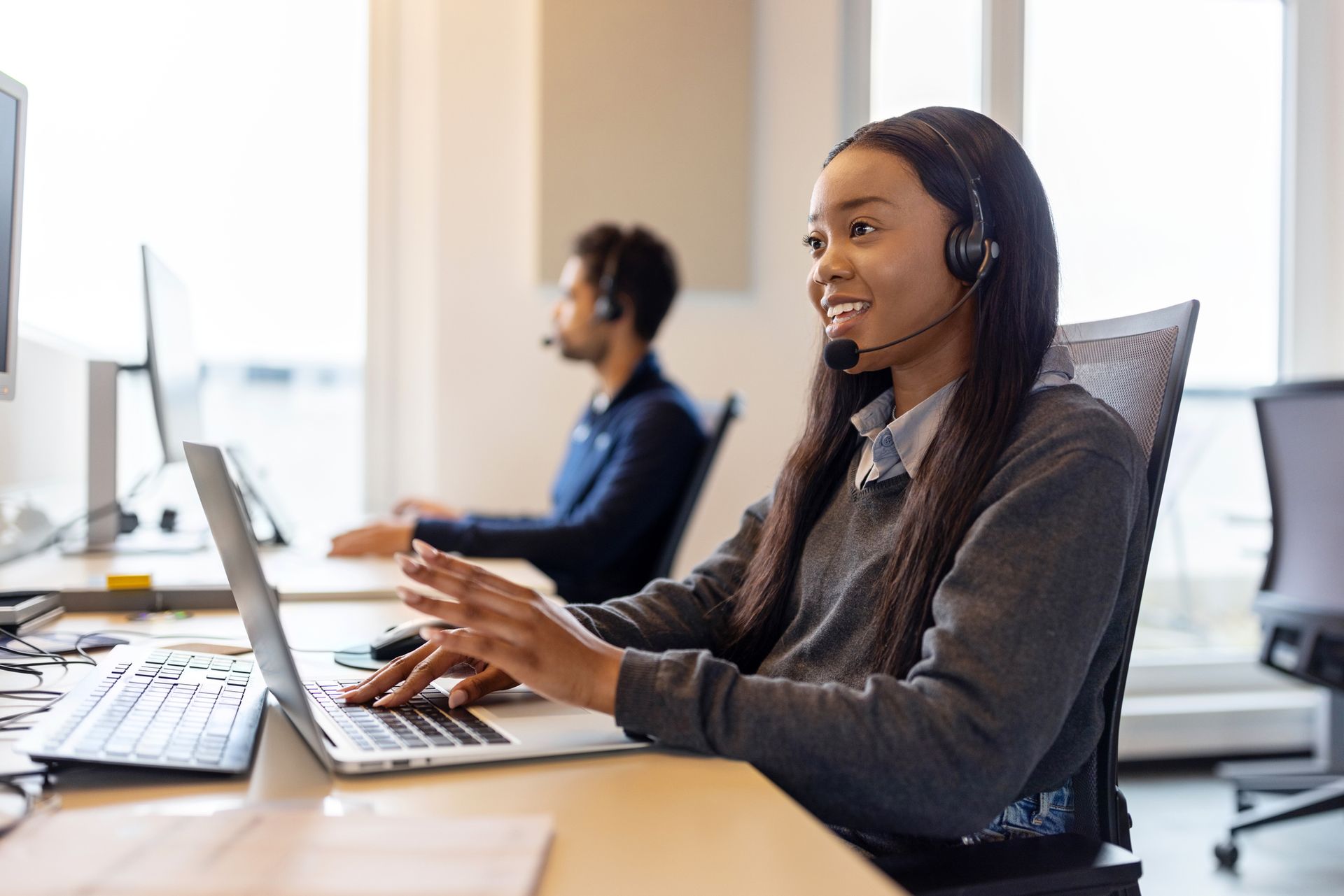 Call center agent working on a laptop with a headset in a modern office setting.