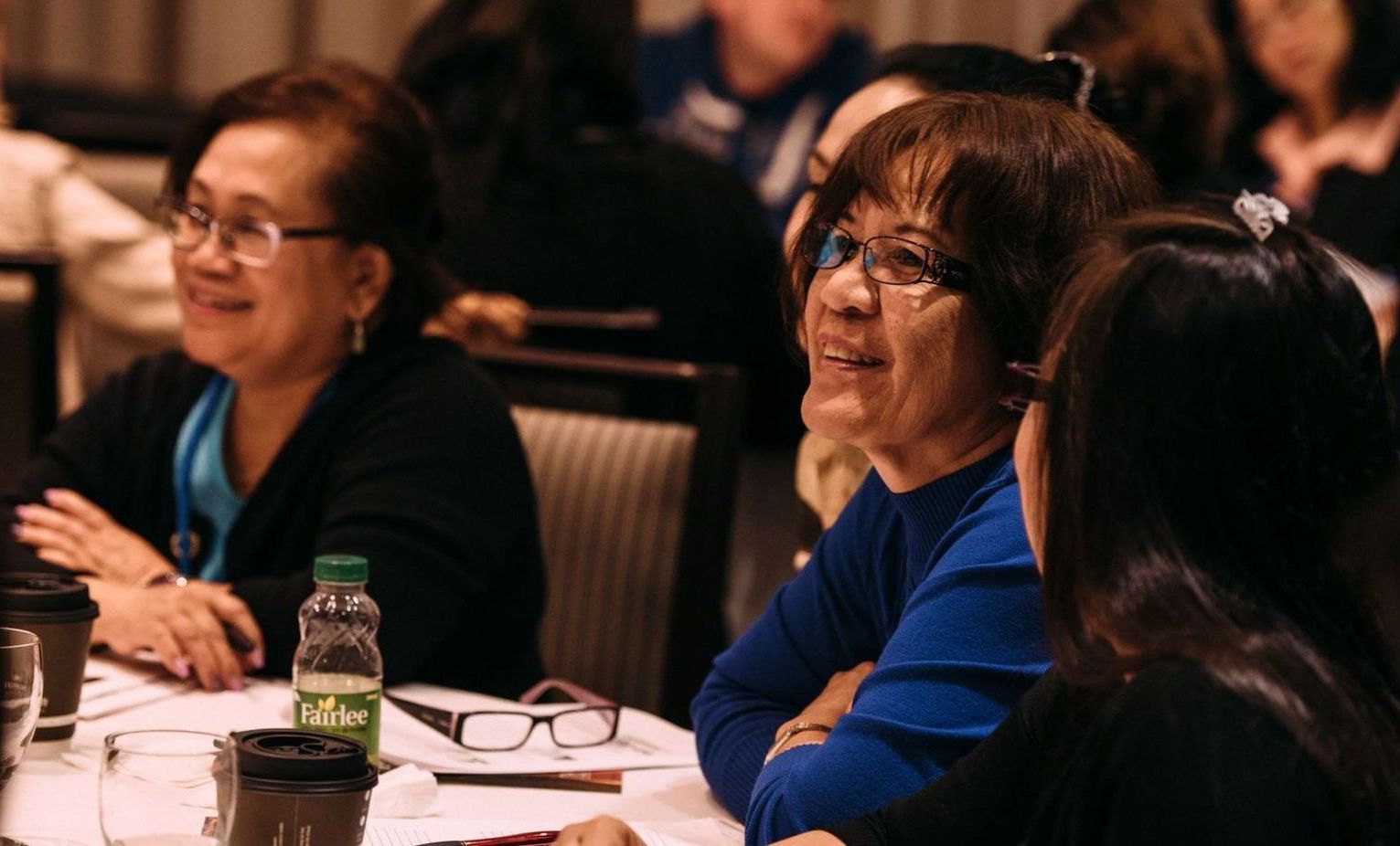 A group of women are sitting at a table talking to each other.