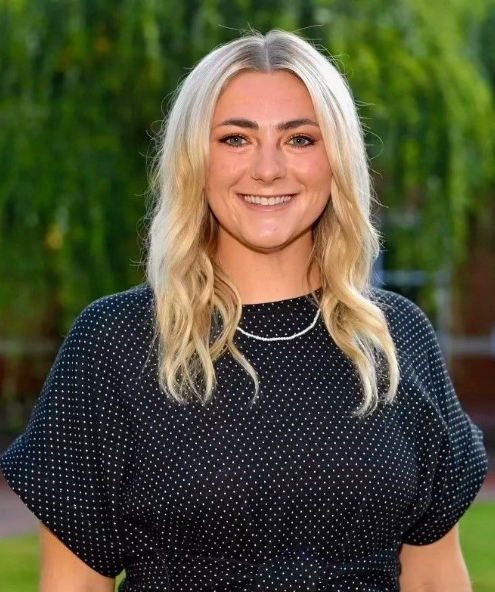 Smiling woman in a black polka-dot top standing outdoors against a blurred green background