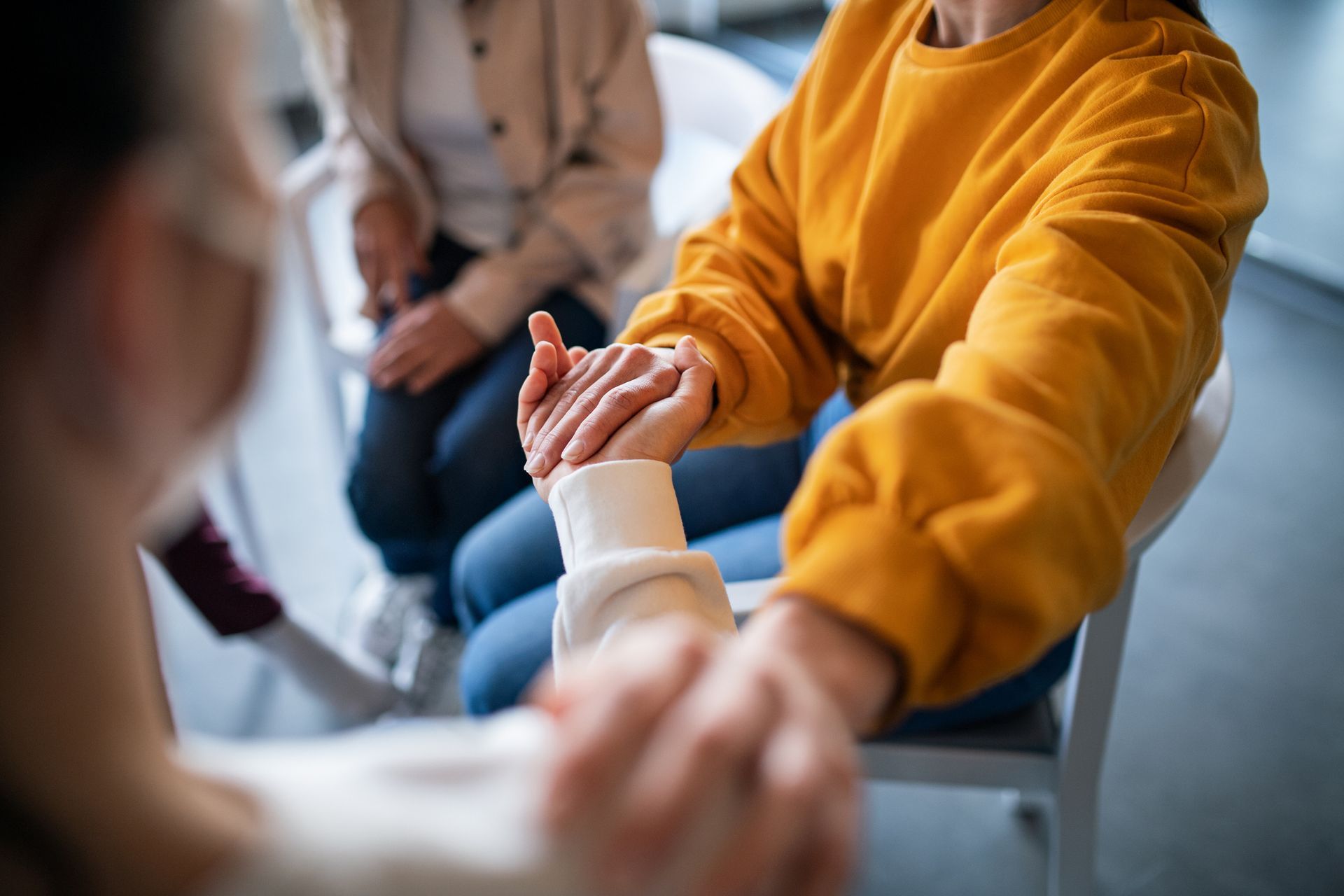 People holding hands in a supportive group circle, with one person in a mustard sweater in focus