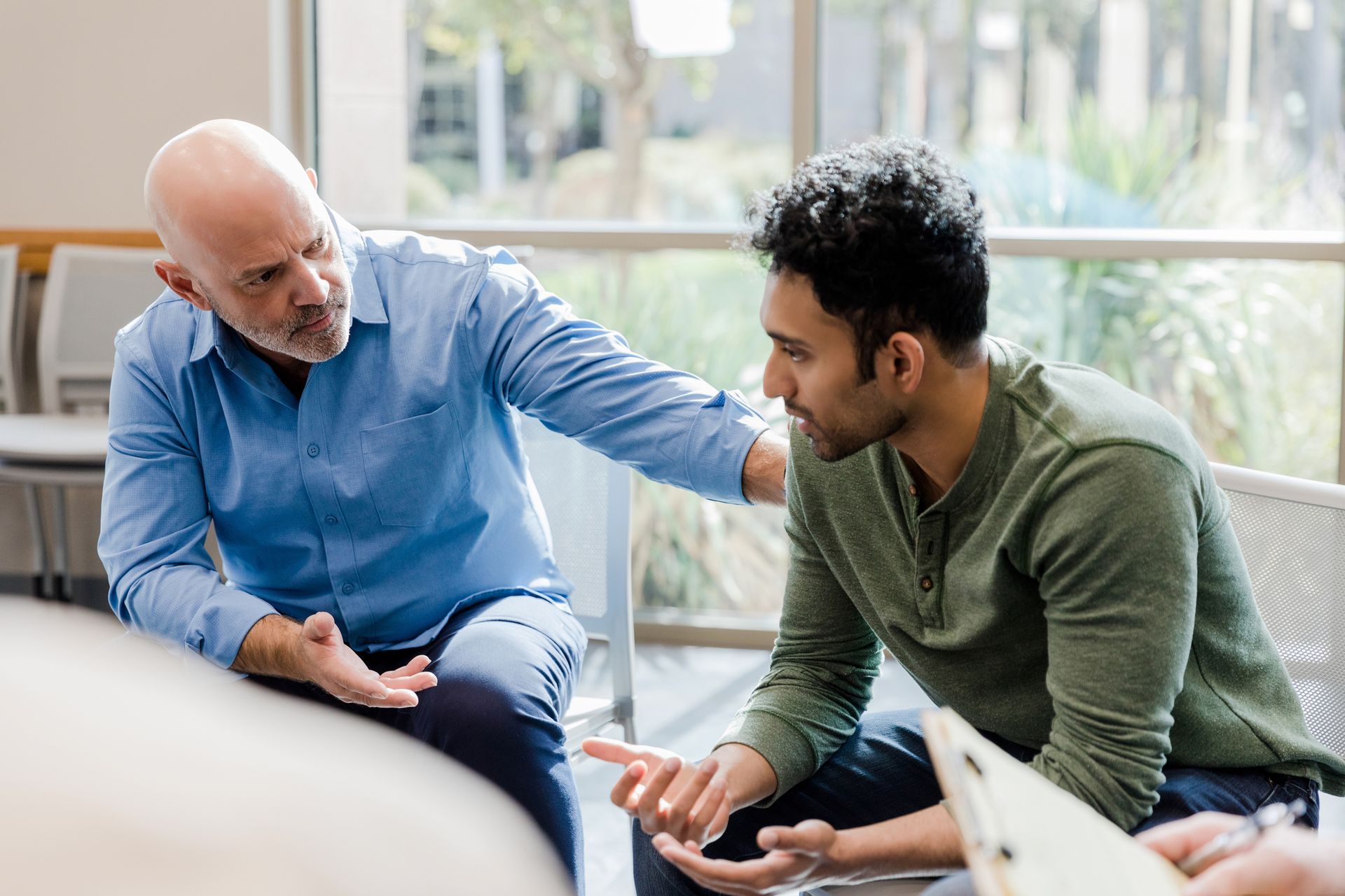 Two men seated on a couch, talking quietly in a bright office lounge