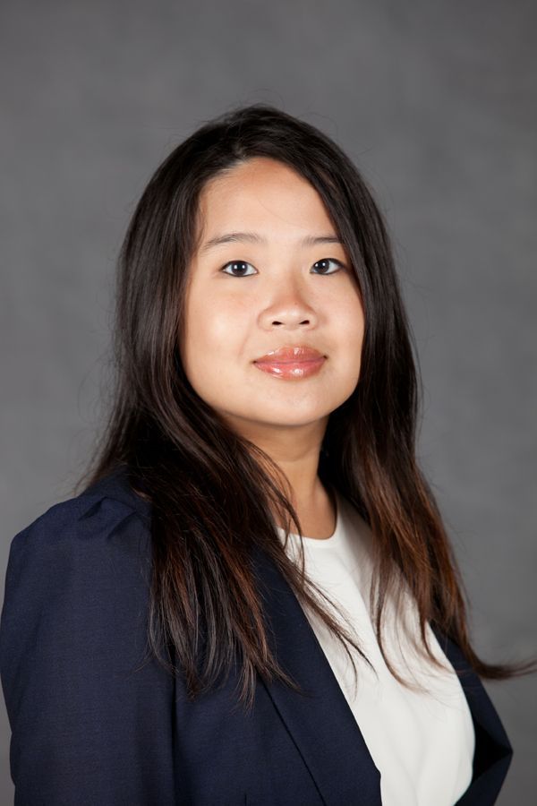 Portrait of a person in a navy blazer and white top against a gray studio backdrop