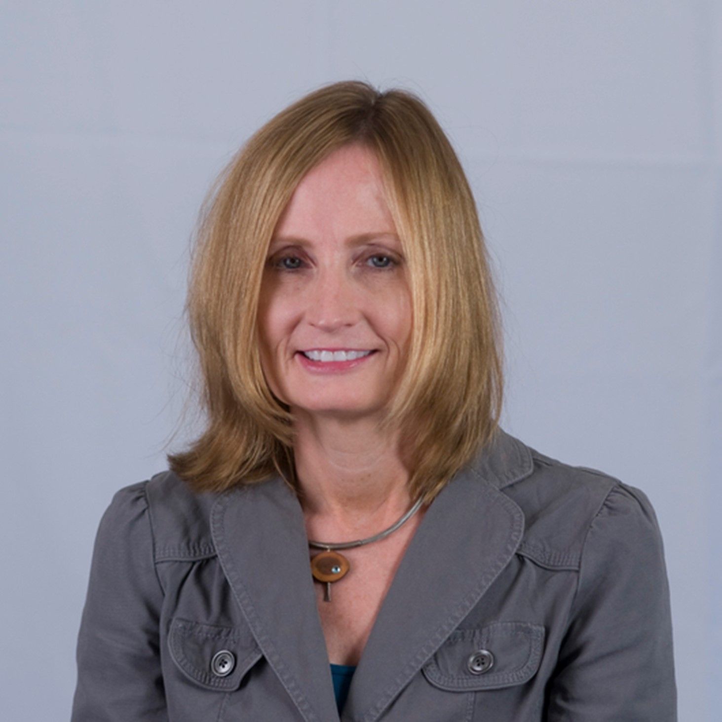 Portrait of a smiling woman in a gray jacket against a light background