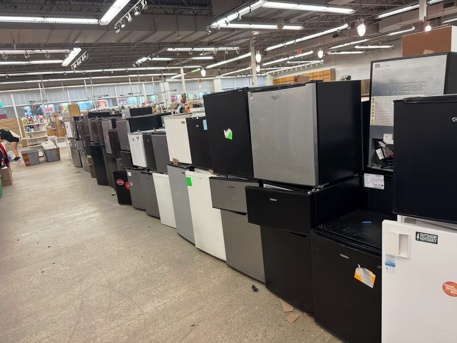 Row of used appliances, mostly washers and dryers, displayed in a large store aisle.