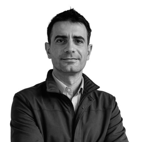 Man in a jacket and button-down shirt, looking directly at the camera, with a neutral expression.