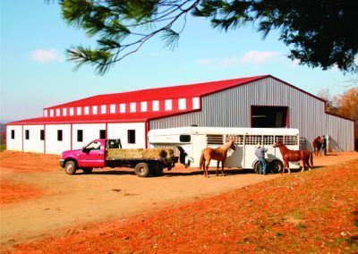 A horse trailer is being pulled by a truck in front of a barn.