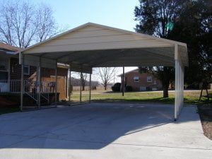 A carport is sitting in the middle of a driveway next to a house.