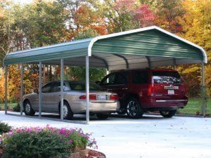 Two cars are parked under a carport in a driveway.