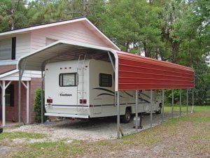 A white rv is parked under a red carport in front of a house.