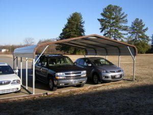 Two cars are parked under a carport in a field.