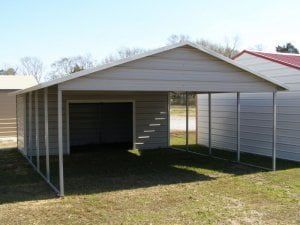 A garage with a carport attached to it is sitting on top of a lush green field.
