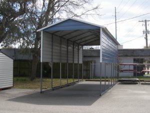 A blue and white carport is sitting in a parking lot next to a shed.