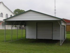 A white garage with a green roof is sitting on top of a lush green field.