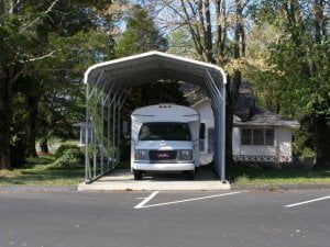A rv is parked under a carport next to a house.