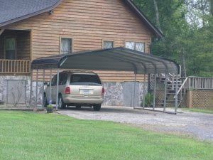 A car is parked under a carport in front of a wooden house.