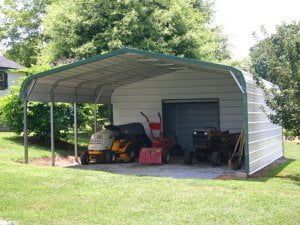 A metal carport with a lawn mower and snow blower inside of it.