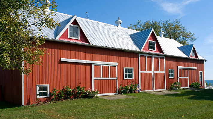 A large red barn with a white roof is sitting in the middle of a grassy field.