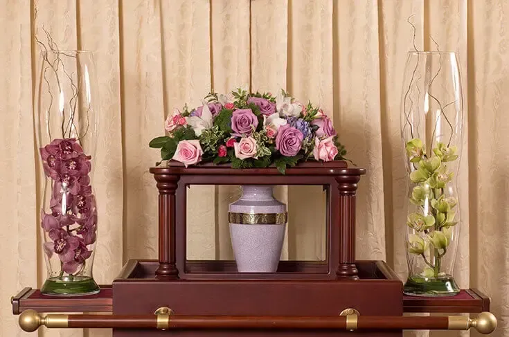A floral arrangement with a decorative urn on a dark wood stand, flanked by tall glass vases with flowers.