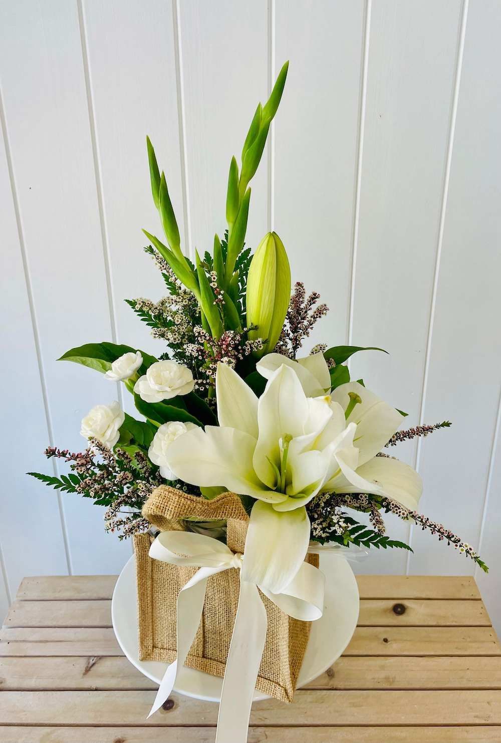 A Vase Filled With White Flowers is Sitting on a Wooden Table — Bundaberg House of Flowers In Coral Cove, QLD