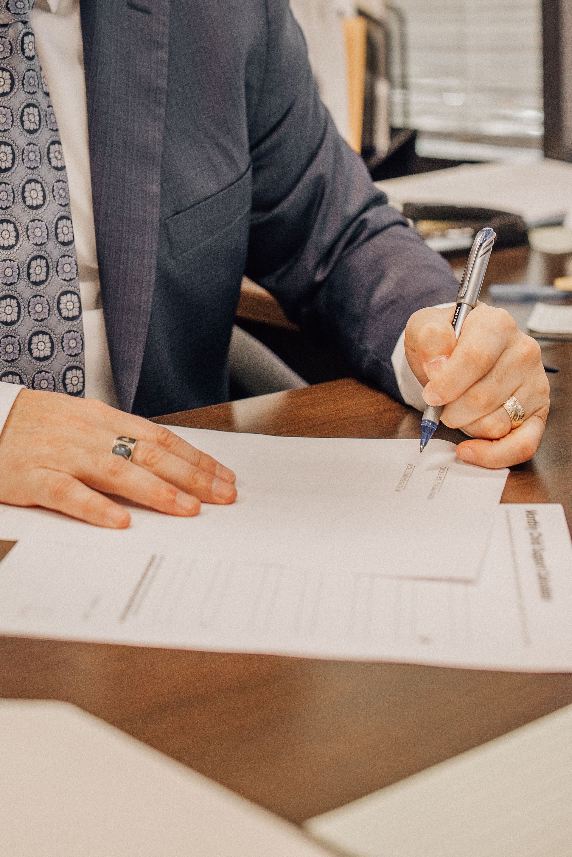 A man in a suit and tie is writing on a piece of paper with a pen.