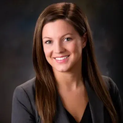 A woman with long brown hair is wearing a gray jacket and smiling for the camera.