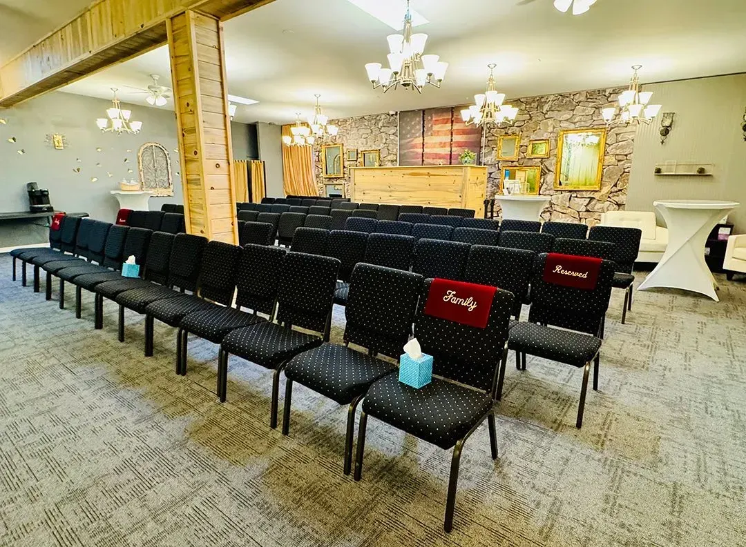 Empty banquet hall with rows of black chairs facing a decorated stage and chandeliers