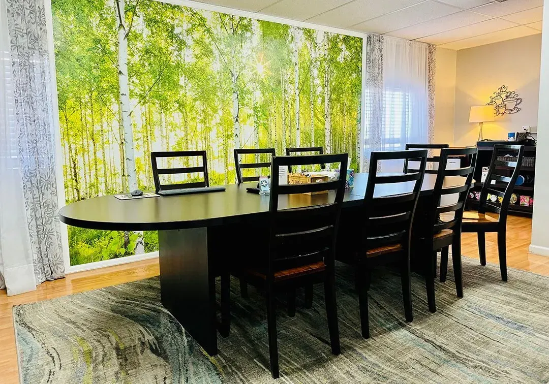 Dining room with a large black table and chairs, bright forest mural, and a floor lamp by the wall.