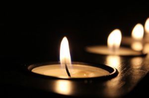 Lit candles glowing in a dark room, with a close-up tealight in the foreground.