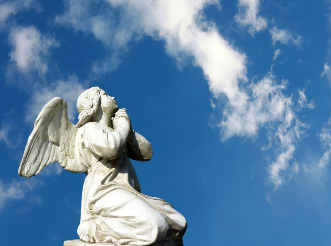 White angel statue kneeling against a blue sky with clouds