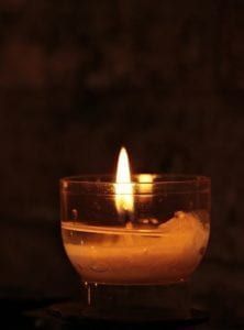 Lit candle in a small glass holder against a dark background