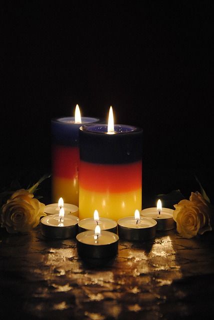Two layered candles glowing on a dark table with tea lights and yellow flowers