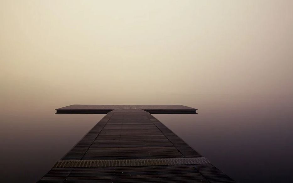 A long wooden dock stretches into a calm, foggy lake at dawn or dusk.