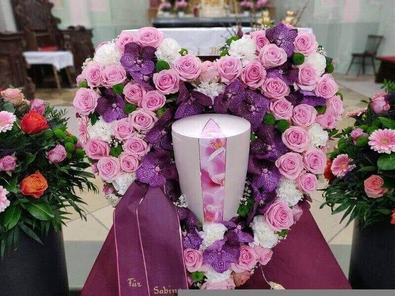 White urn framed by purple and pink rose wreaths at a funeral display