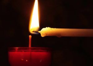 Lit candle flame touching the wick of another candle on a dark background