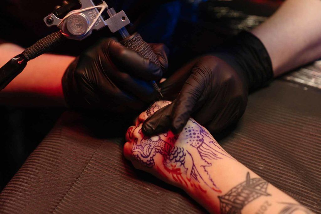 Gloved tattoo artist tattooing a hand with a red rose design on a tattoo table