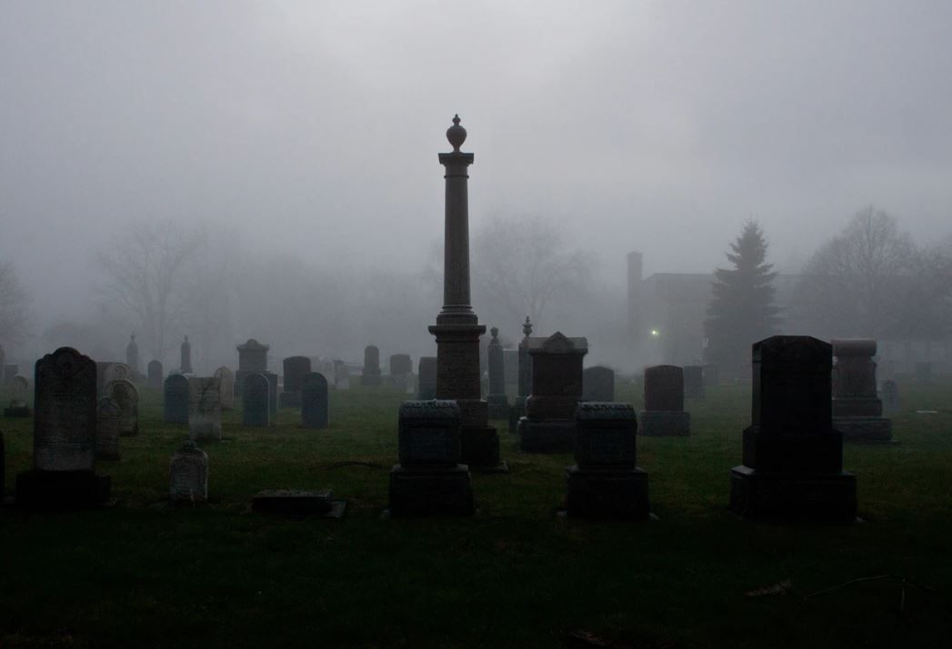 Foggy cemetery with gravestones and a tall monument at the center