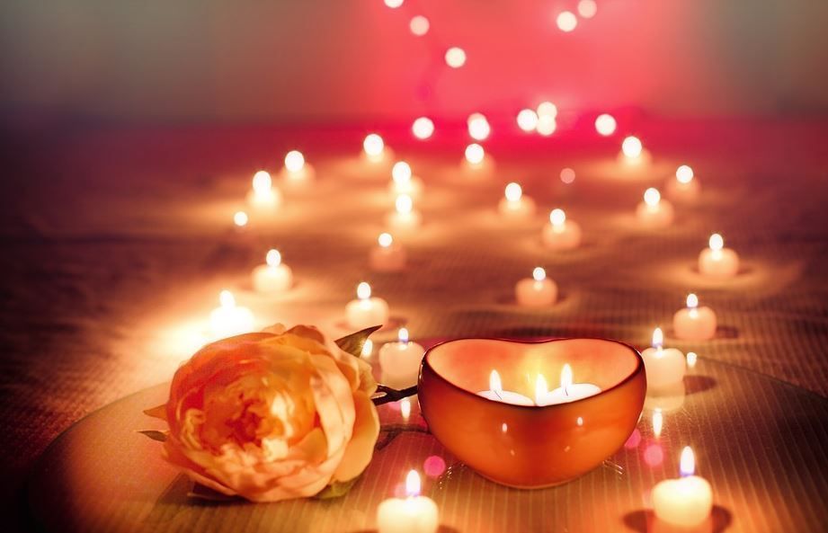 Candlelit spa scene with a rose and glowing tea light candles on a wooden surface