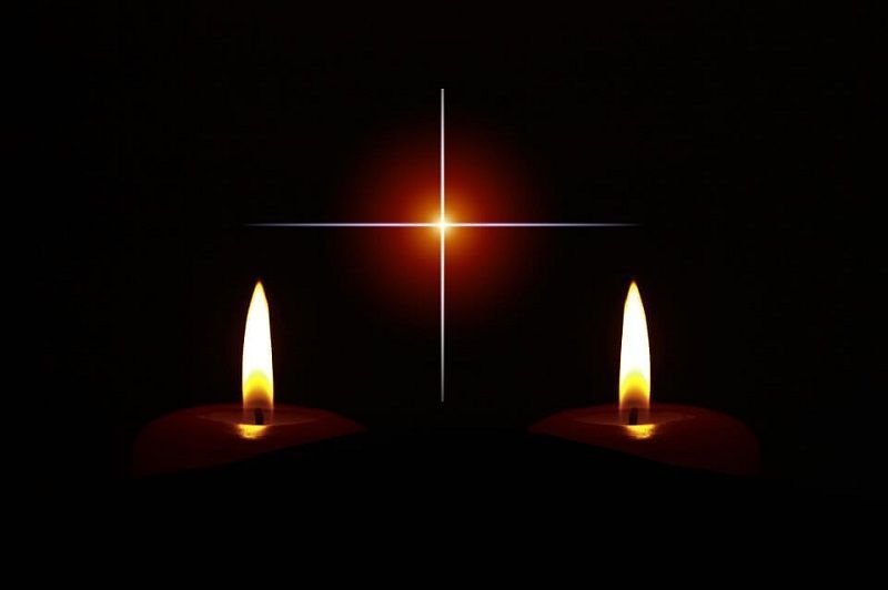 Two lit candles with a glowing star-like light in the dark background