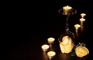 Candles and white roses arranged on a dark surface in low light