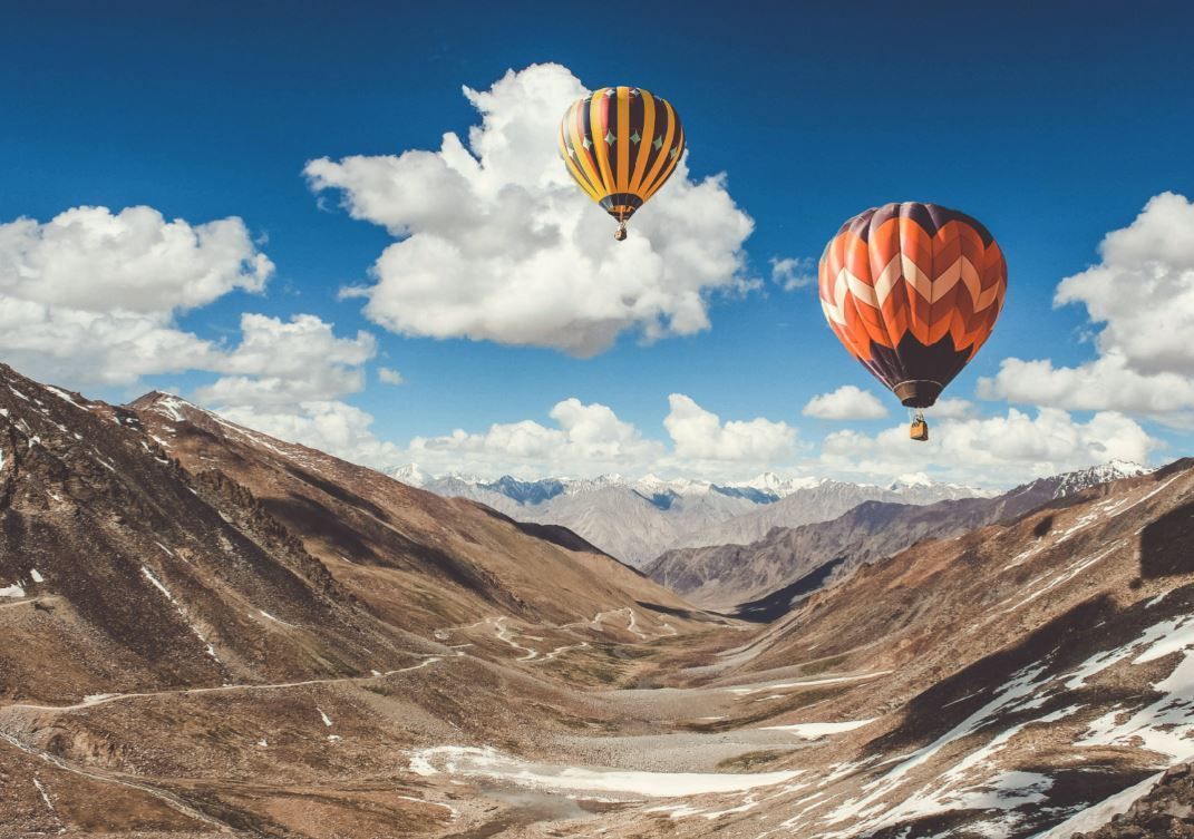 Two hot air balloons over a snowy mountain valley under a blue sky