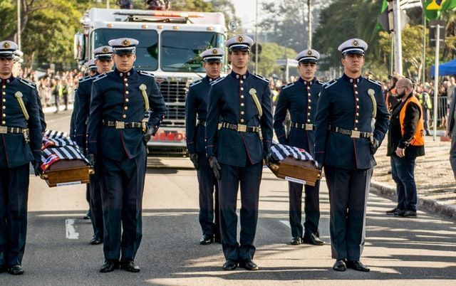 Uniformed honor guard carrying a flag-draped casket during a funeral procession outdoors