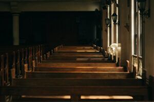 Empty wooden church pews in a dimly lit aisle with sunlight streaming through windows