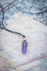 Purple crystal pendant on a black cord against a light stone background
