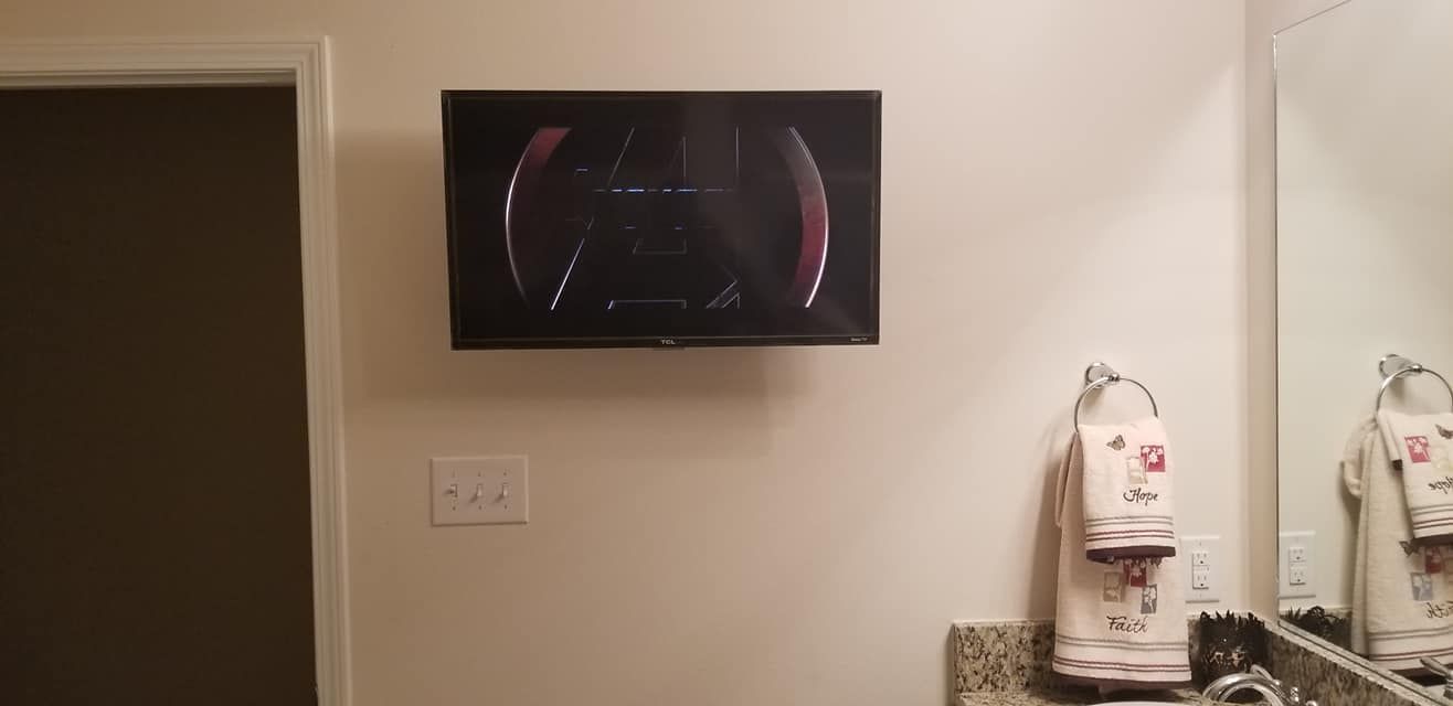 A bathroom with a television mounted on the wall above the sink.
