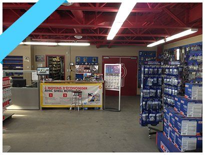 Allée d'un magasin de quincaillerie avec des étagères de produits en boîte et un comptoir éclairé par des néons puissants.