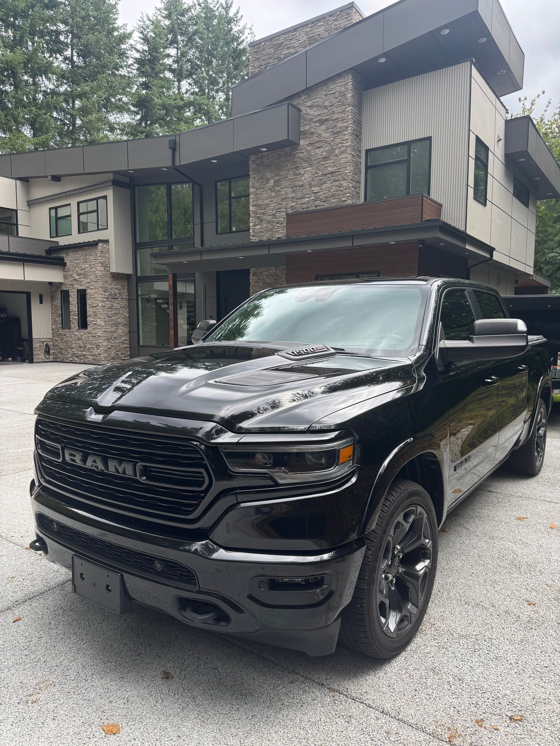 Black pickup truck parked in front of a modern house on a wet driveway, surrounded by trees. | Lapin Auto Repair